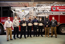 A group of firefighters standing in front of a fire truck with masks and certificates