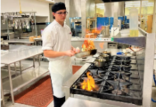 student with chef jacket and hat with pan and flames