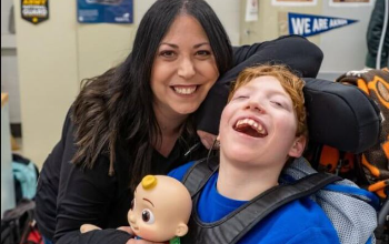 child in wheelchair smiling with his mom holding a toy
