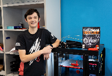Student smiling leaning against 3d printer with magazine