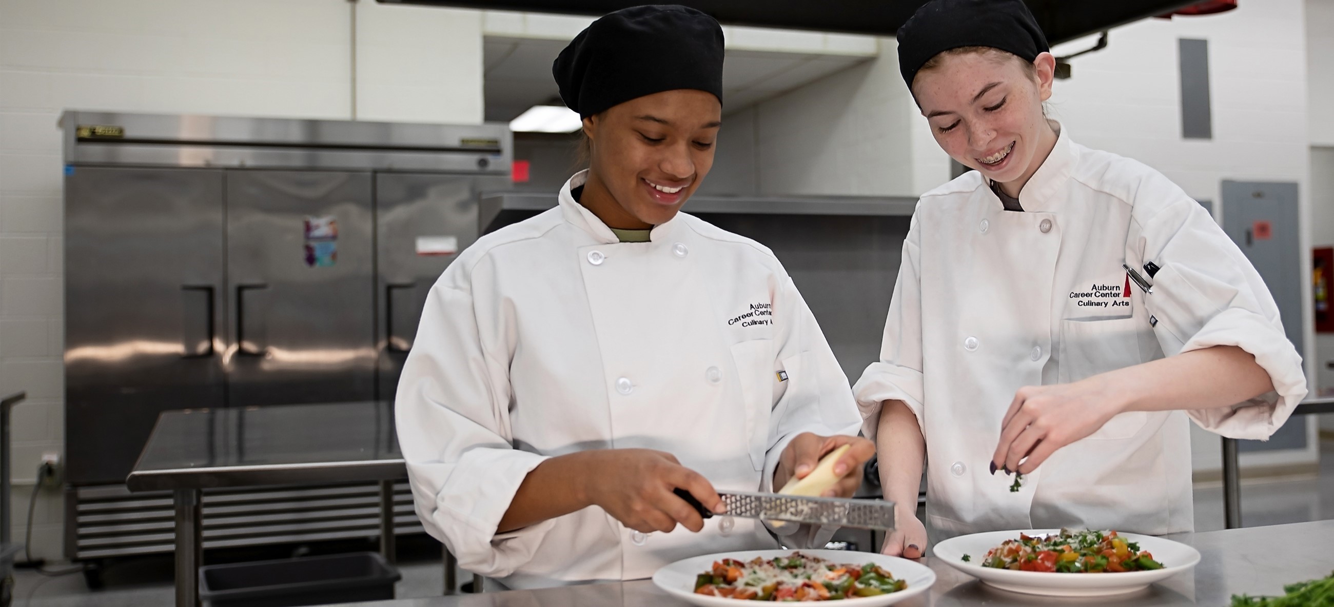 Two culinary students smiling and garnishing dishes