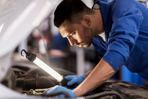 man looking under the hood of a car with a light